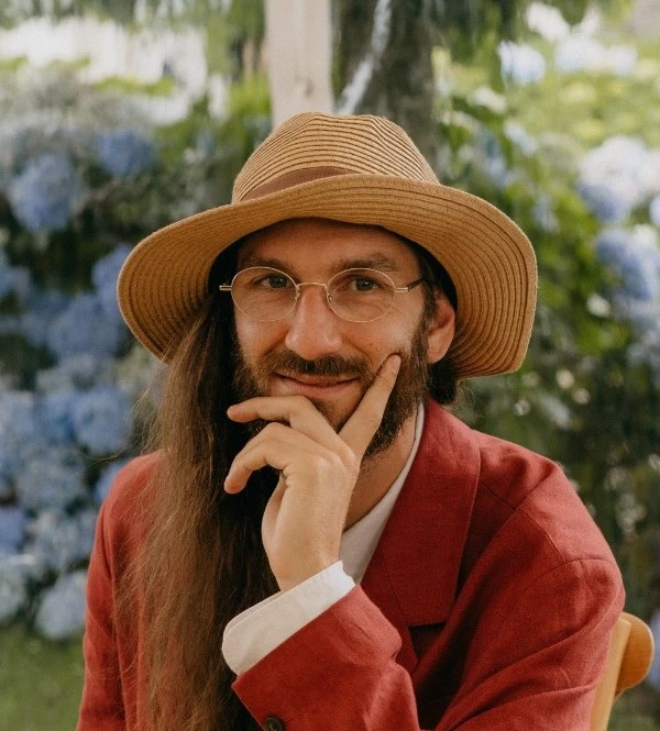 Portrait of Antoine Bellemare-Pepin in a straw hat and a red linen jacket, before blue hydrangeas.